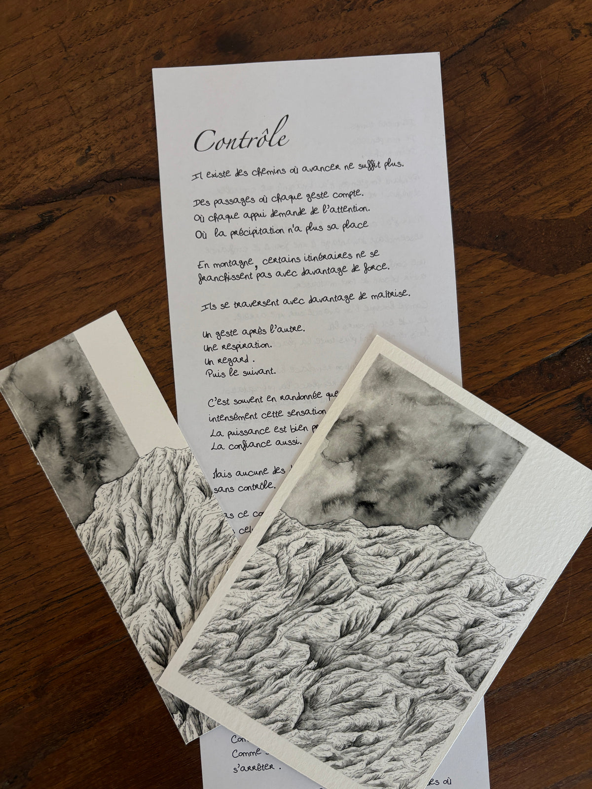 Cette image présente une partie du contenu de la correspondance à l'encre des cimes réalisées par Coline Pratviel, on peut voir sur une table en bois un extrait de la lettre du mois, le tirage d'art de montagne représentant le sentiment de contrôle au format 10x15 cm ainsi que le marque page