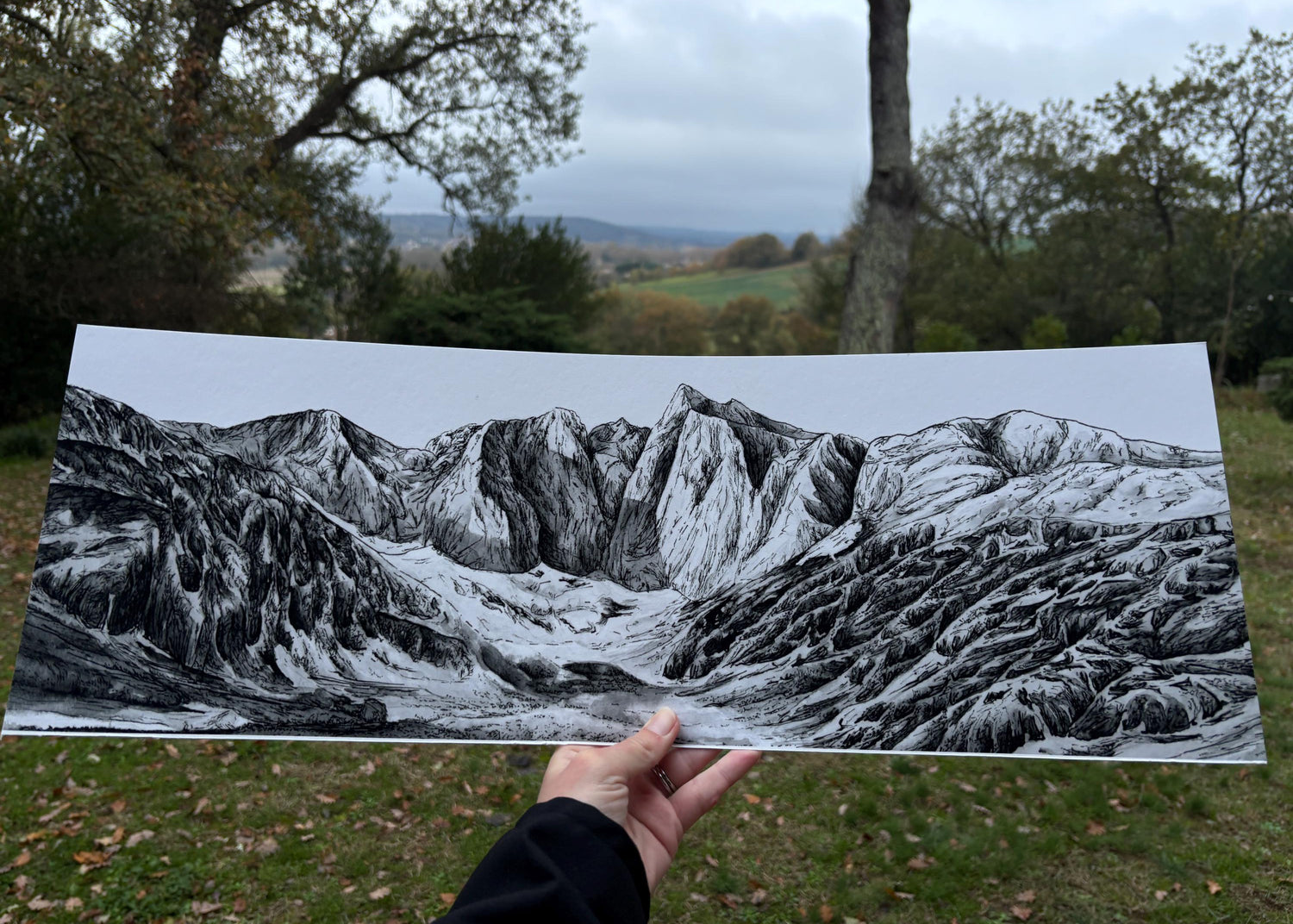 Tirage d'art du Vignemale au format panoramique et aux dimensions de 20 par 60 cm, tenu par ma main dans la nature devant un ciel nuageux, une représentation brute de la nature et des paysages emblématiques des Pyrénées