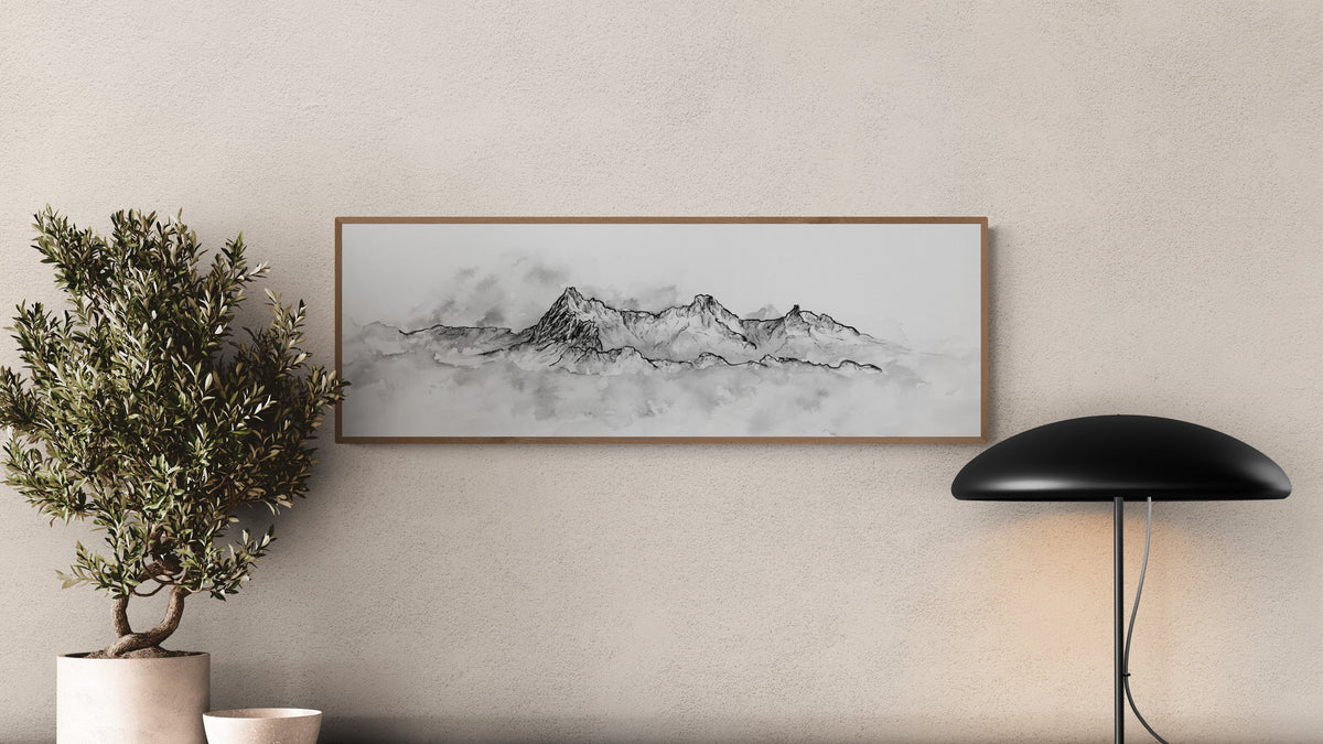 Peinture à l'encre de chine, monochrome d'une montagne qui apparait à travers les nuages, affichée au-dessus d'une table d'entrée ou de salon en bois naturel.  Peinture en noir et blanc de montagne et de nature, le tirage d art est encadré dans un cadre en bois, tirage fine art de qualité muséale, art pour les amoureux de la nature, montagne noir et blanc. Le tableau est affiché à côté d'un olivier ajoutant une touche de décoration esthétique et naturelle à cette décoration d'intérieur.
