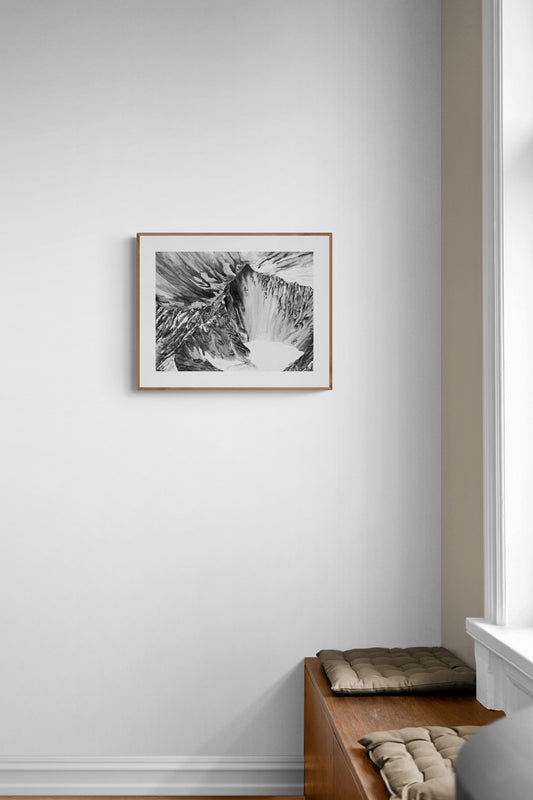 Tirage d'art de l’Obergabelhorn au format A4 en noir et blanc encadré dans un cadre en bois au-dessus d'un banc en bois. Lumière naturelle sur l'affiche. Décoration murale artisanale et naturelle