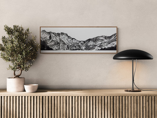 Peinture à l'encre de chine, monochrome du Massif du Néouvielle affiché au-dessus d'une table d'entrée ou de salon en bois naturel.  Peinture en noir et blanc de montagnes et de nature, le tirage d'art est encadré dans un cadre en bois, tirage fine art de qualité muséale, art pour les amoureux de la nature, montagne noir et blanc, Pic Français. Le tableau est affiché à côté d'un olivier et d'une lampe, ajoutant une touche de décoration esthétique et naturelle à cette décoration d'intérieur.